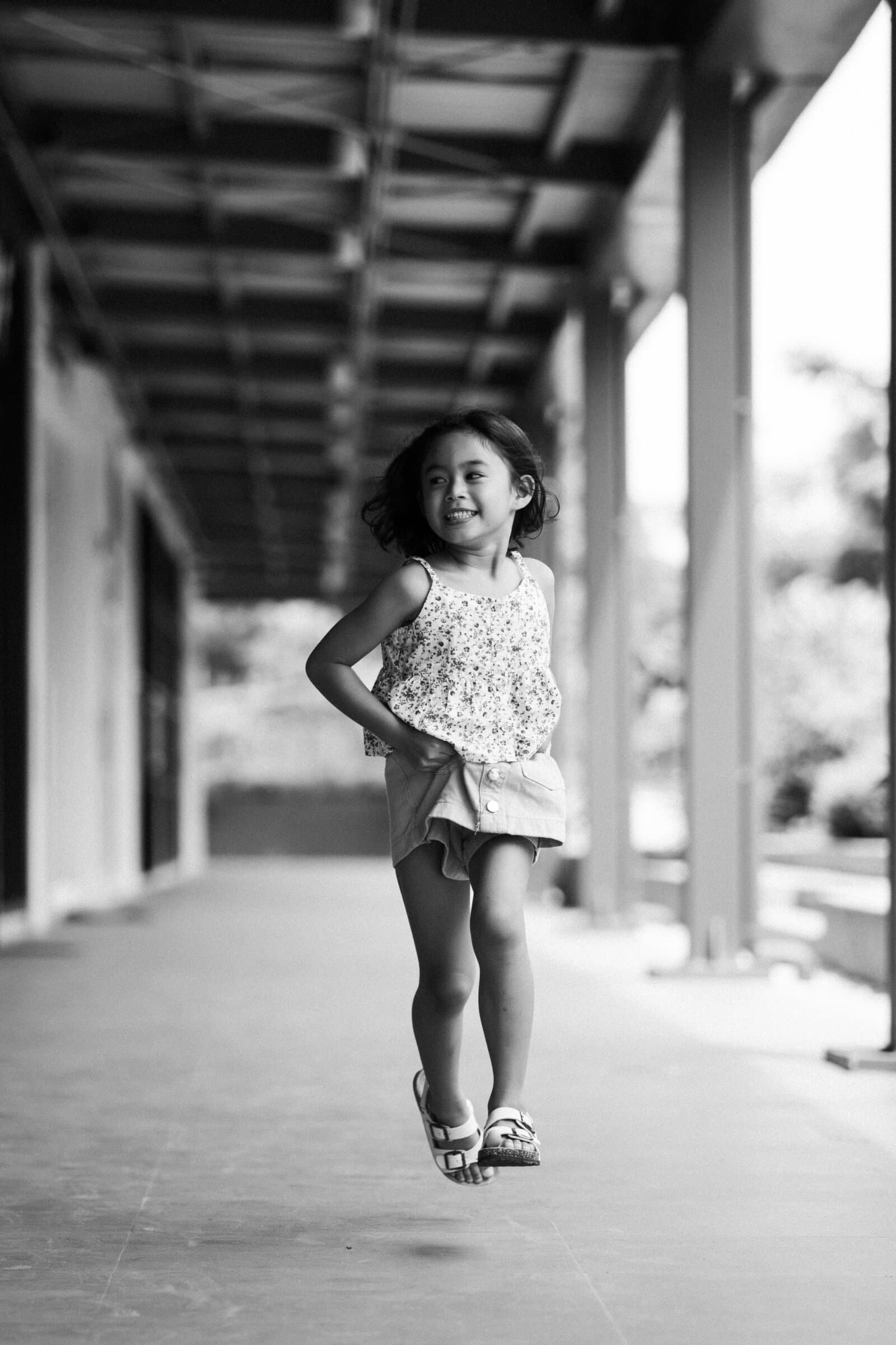 Girl skipping along a covered walkway, black and white