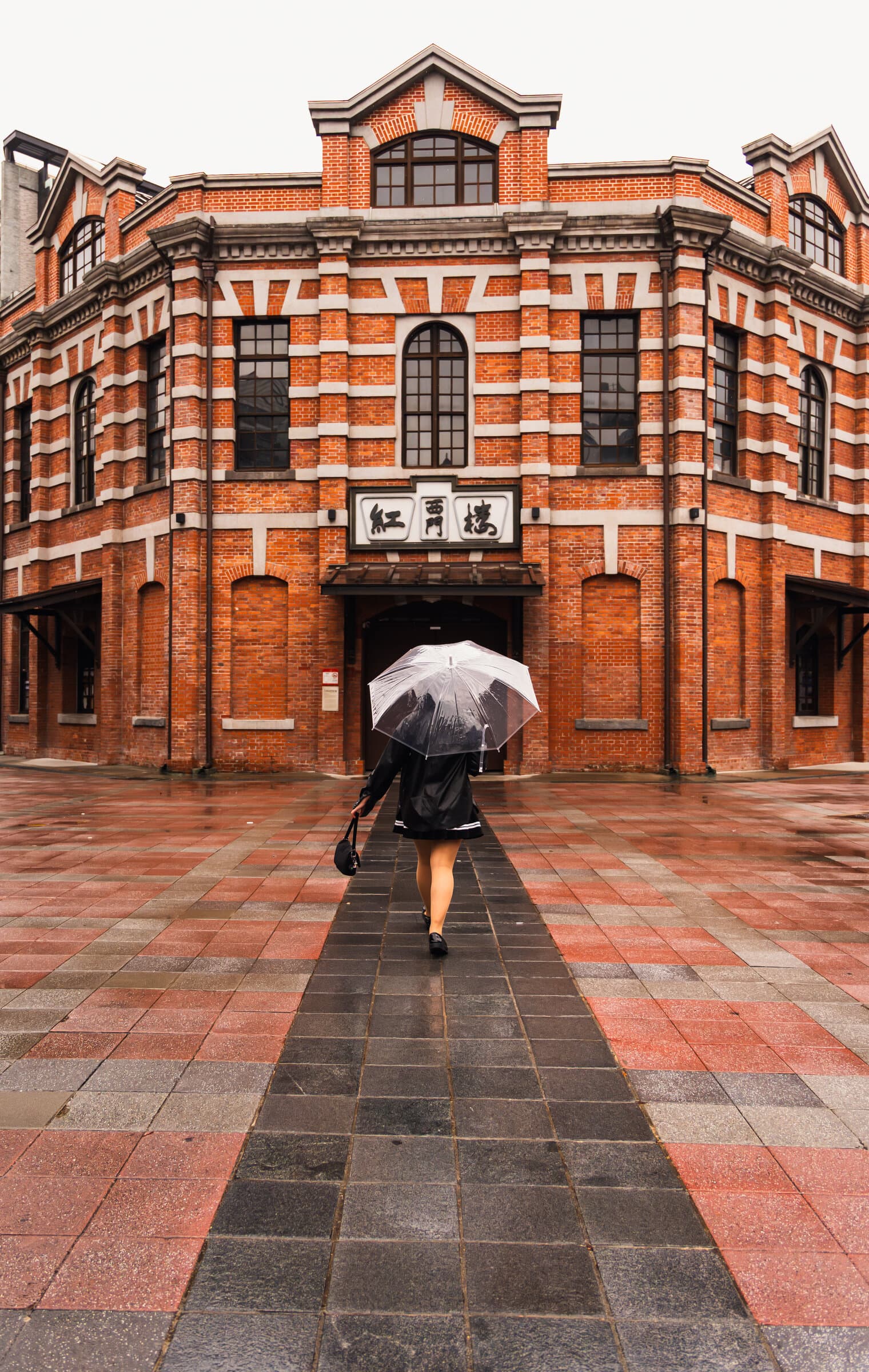 Umbrella crossing a red-brick courtyard in the rain